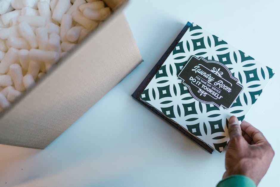 Mão segurando caixa com material de embalagem e cartão personalizado para marca pessoal.