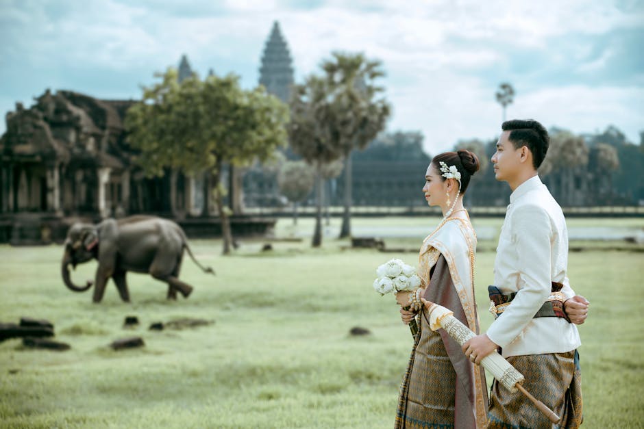 Casal cambojano elegante em trajes tradicionais em Angkor Wat, com um elefante ao fundo, representando a conexão entre a cultura e o bem-estar.