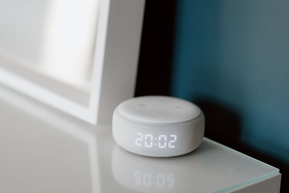 Smart speaker com display de LED mostrando 20:02, sobre uma mesa.