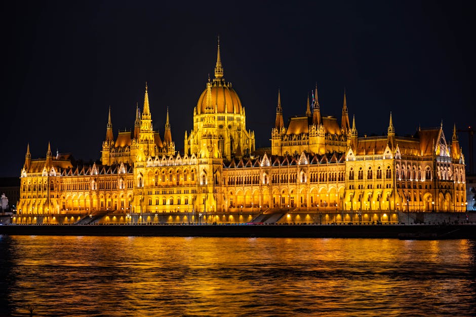 Parlamento de Budapeste iluminado refletindo no Rio Danúbio à noite.