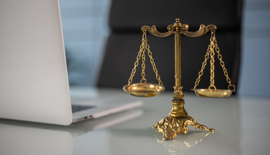 Uma balança dourada de justiça em cima de uma mesa ao lado de um laptop, simbolizando lei e equilíbrio.