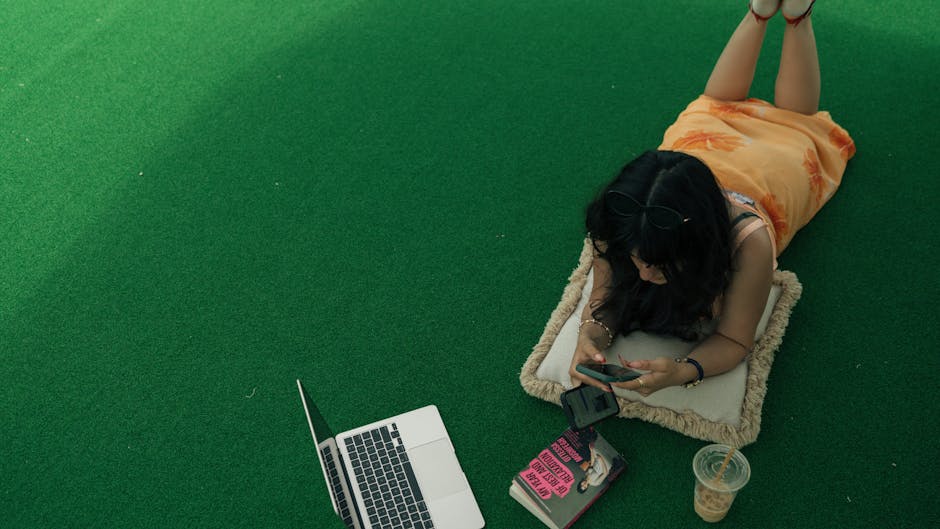 Mulher estudando ao ar livre com celular, laptop e livro para educação online.