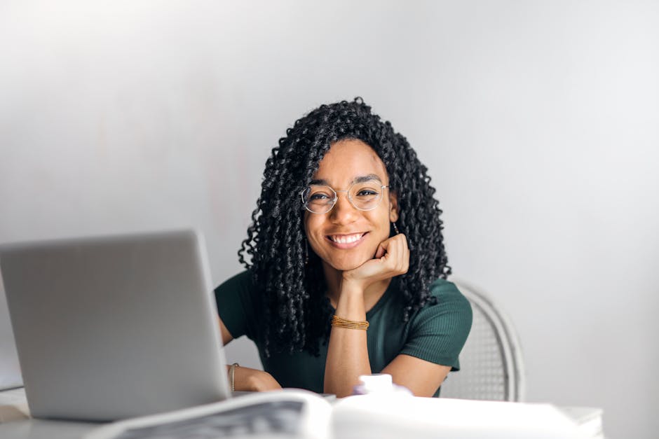 Mulher sorridente com cabelos cacheados usando laptop para estudar online em ambiente interno.