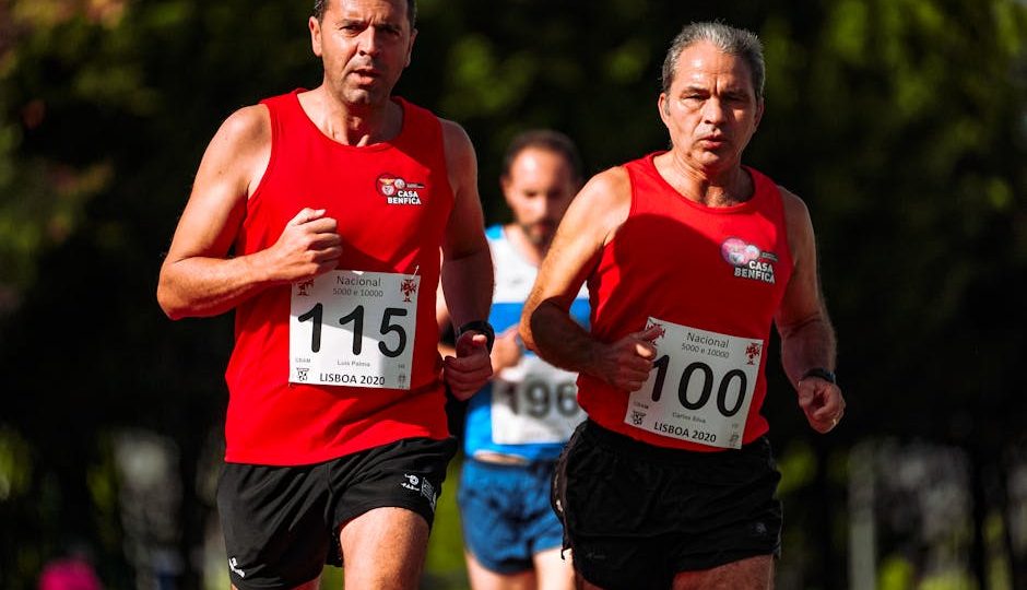 Dois homens de meia-idade em camisetas vermelhas correndo em uma competição de maratona ao ar livre.