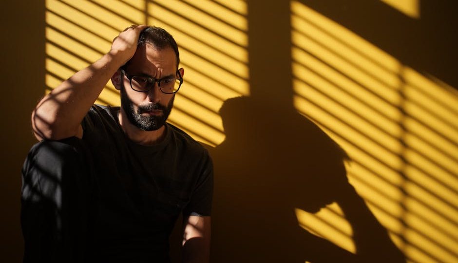 Homem contemplativo em ambiente sombrio, expressão pensativa.