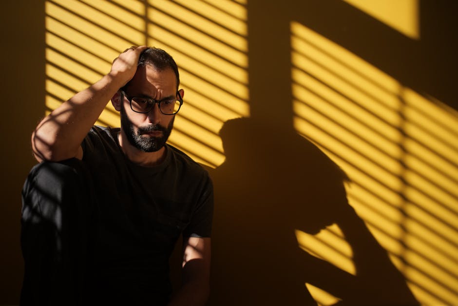 Homem contemplativo em cena interna com sombras dramáticas, retratando a saúde mental.