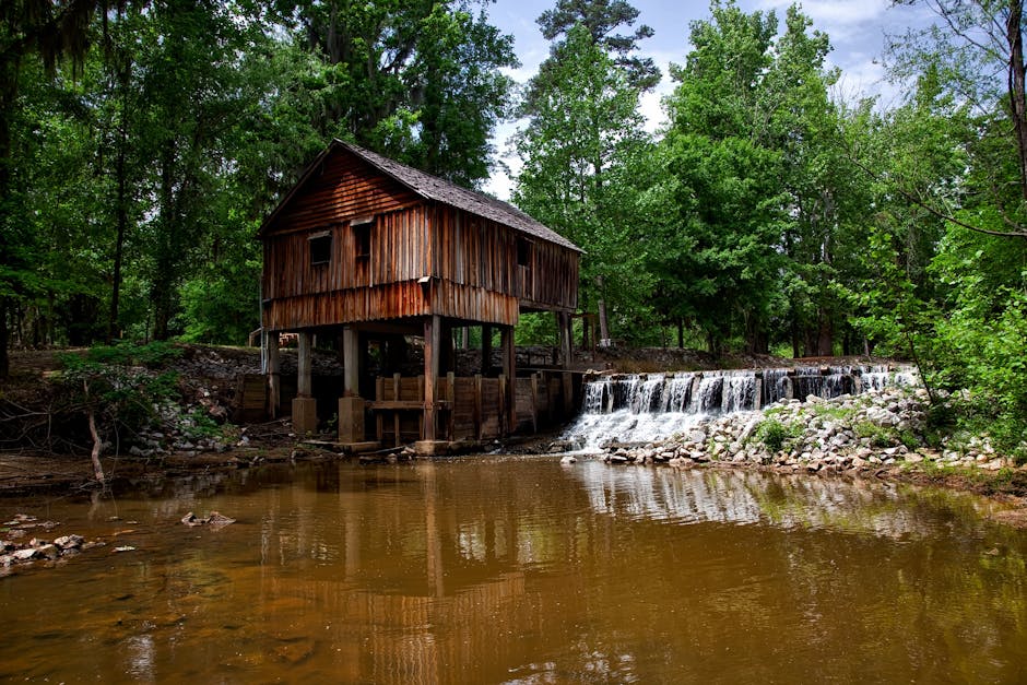 Moinho de madeira histórico em Alabama, cercado por uma cachoeira serena e uma floresta verde exuberante.