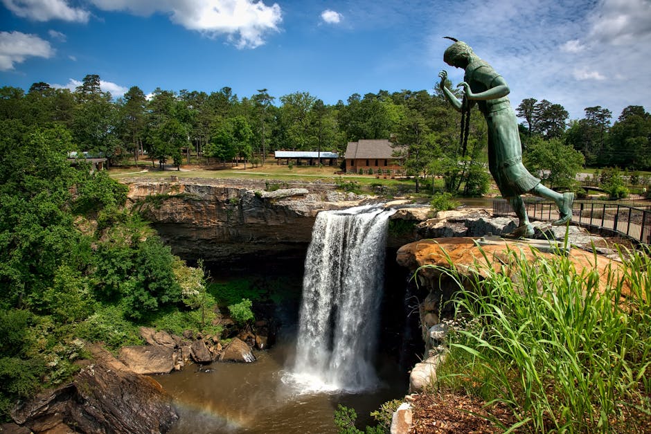 Uma vista deslumbrante das Cataratas Noccalula com uma estátua histórica em meio a vegetação exuberante sob um céu brilhante.