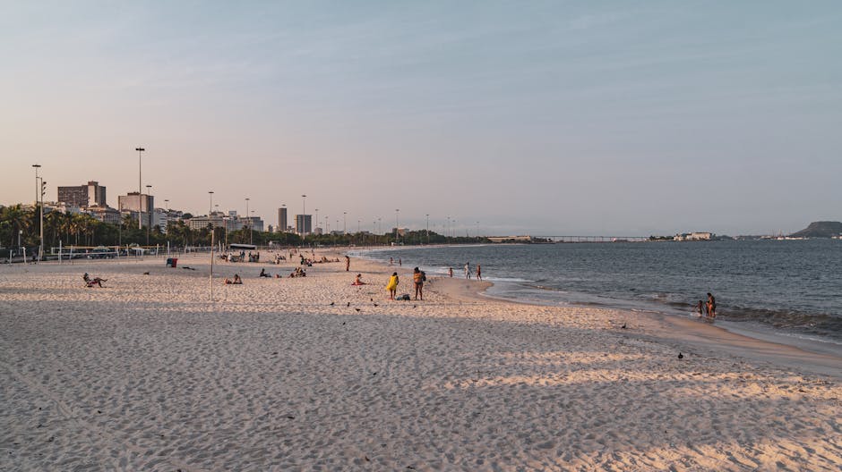 Pessoas curtindo o dia ensolarado na Praia do Flamengo, no Rio de Janeiro, com vista da skyline da cidade.