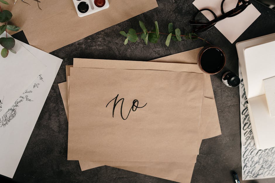 Papel com a palavra 'não' escrita em caligrafia, tinta e folhas de eucalipto dispostos em flat lay estético.