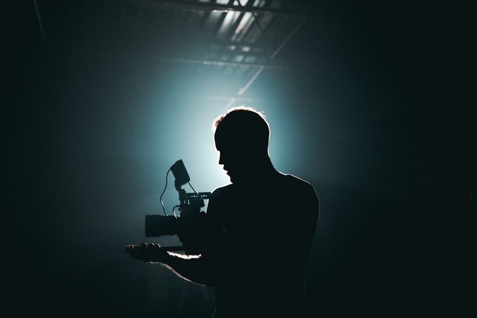 Fotógrafo de cinema em silhueta com equipamento de câmera em ambiente dramático e pouca luz.