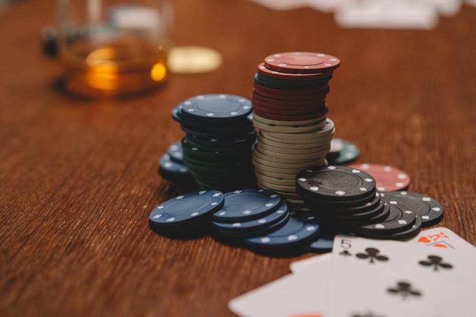 Fichas de pôquer empilhadas em uma mesa de madeira com cartas de baralho e copo desfocado ao fundo.