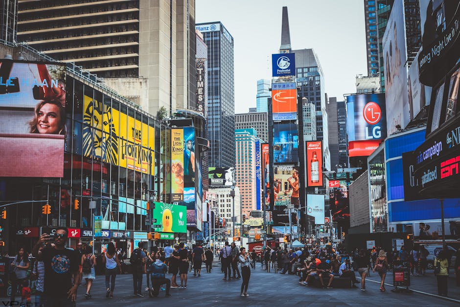 Movimentada vista diurna da Times Square com multidões, arranha-céus e icônicos painéis publicitários em Nova York.