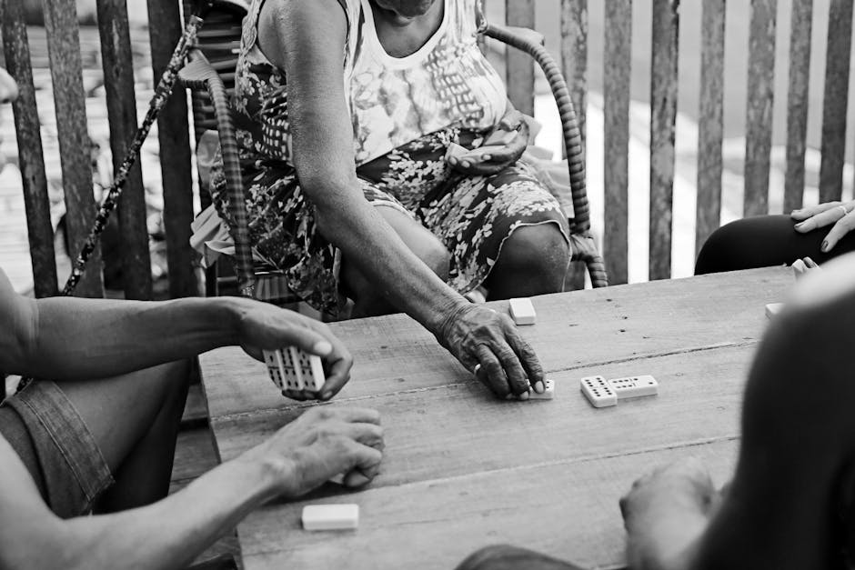 Foto em preto e branco de pessoas jogando dominó em uma mesa de madeira no sertão brasileiro.