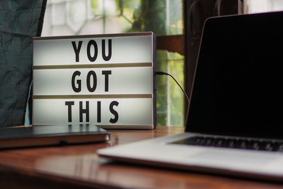 Placa iluminada com 'Você Consegue' ao lado de laptop em mesa de escritório.